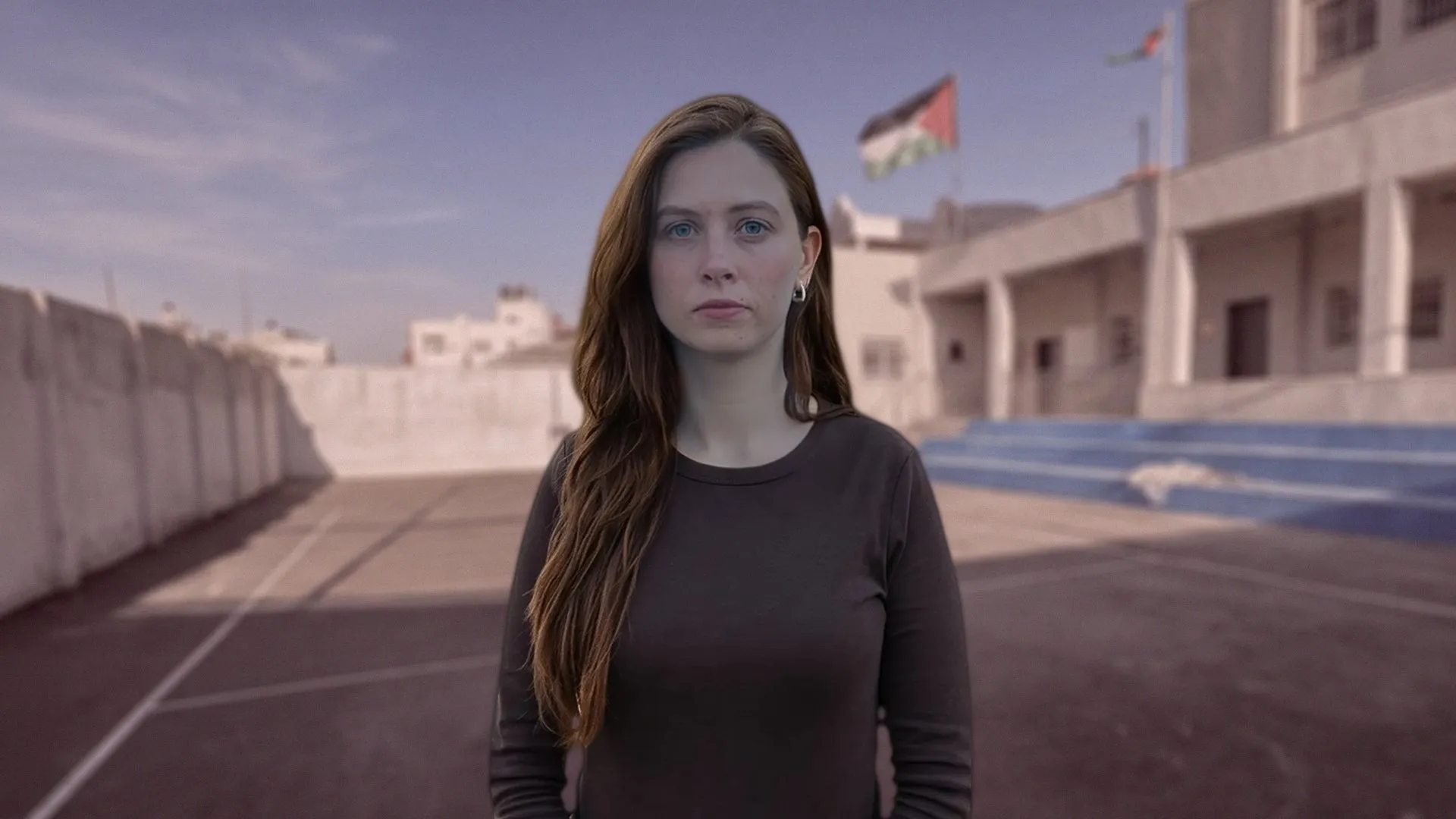 Woman standing on a rooftop beside buildings, with a Palestinian flag visible in the background