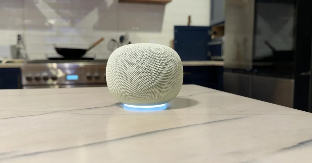 White smart speaker glowing blue on a marble kitchen island, with blurred appliances behind it
