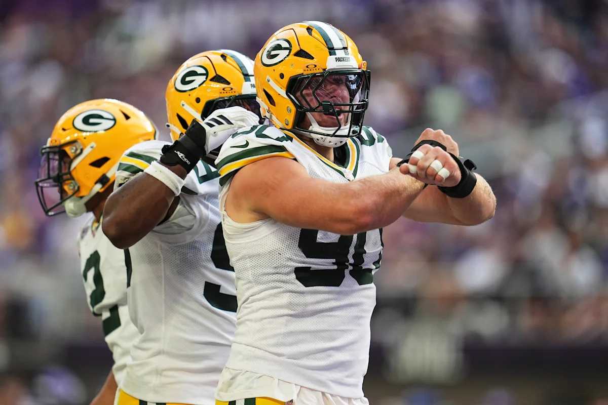 Three Green Bay Packers players in helmets and uniforms perform a blocking drill on the field.