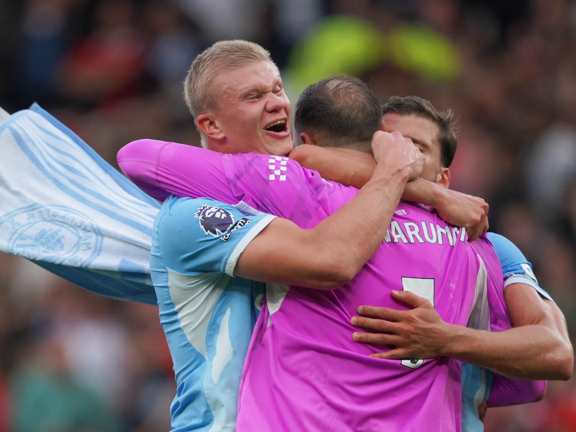 Football players embrace and celebrate during a match, with supporters blurred in the background.