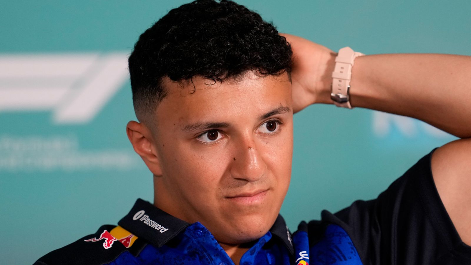 Portrait of a young man in a blue racing suit, raising one arm against a teal background.
