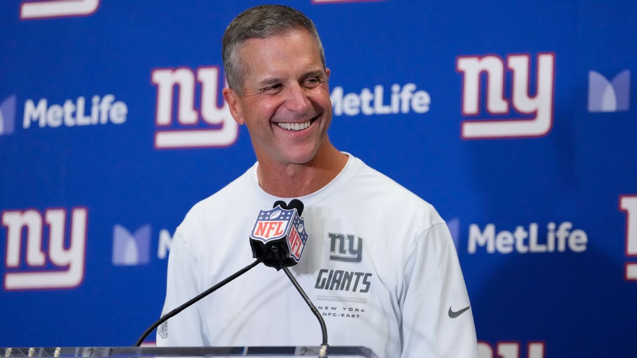 Smiling man in Giants sweatshirt speaks at a podium during a press conference.
