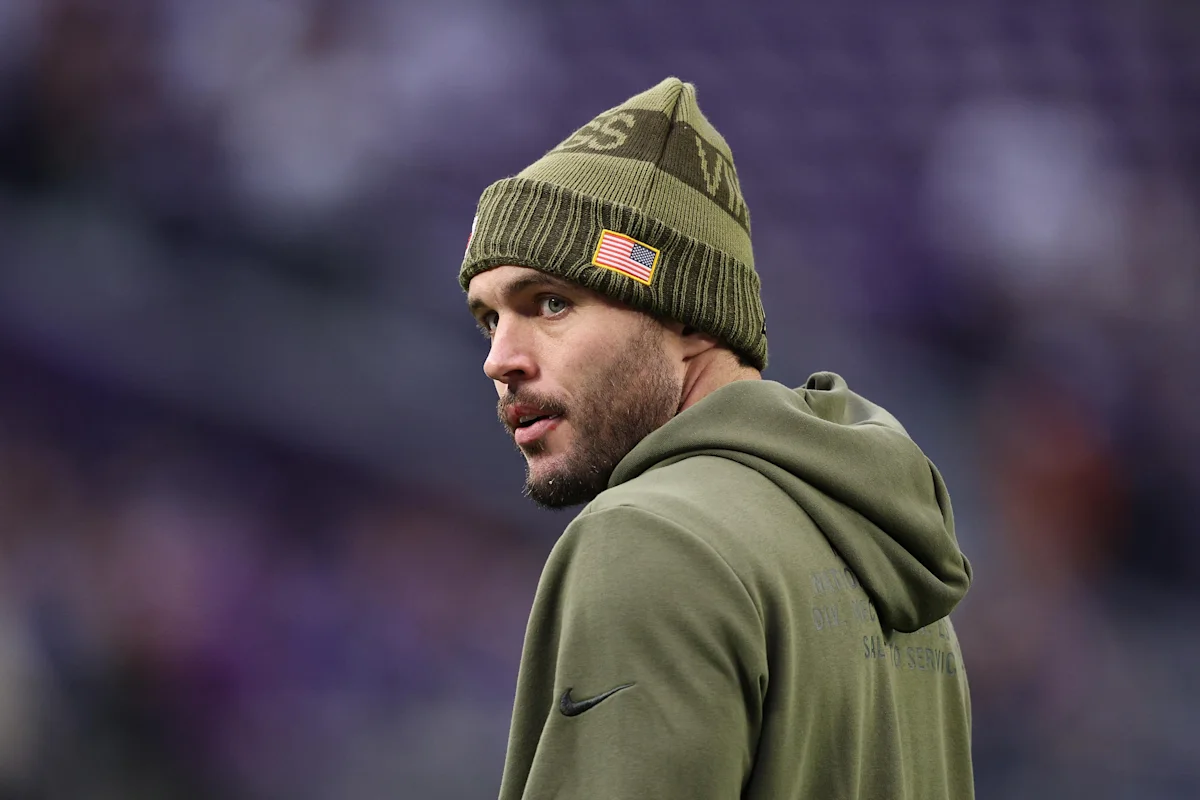Bearded football player wearing an olive beanie and hoodie looks over his shoulder.