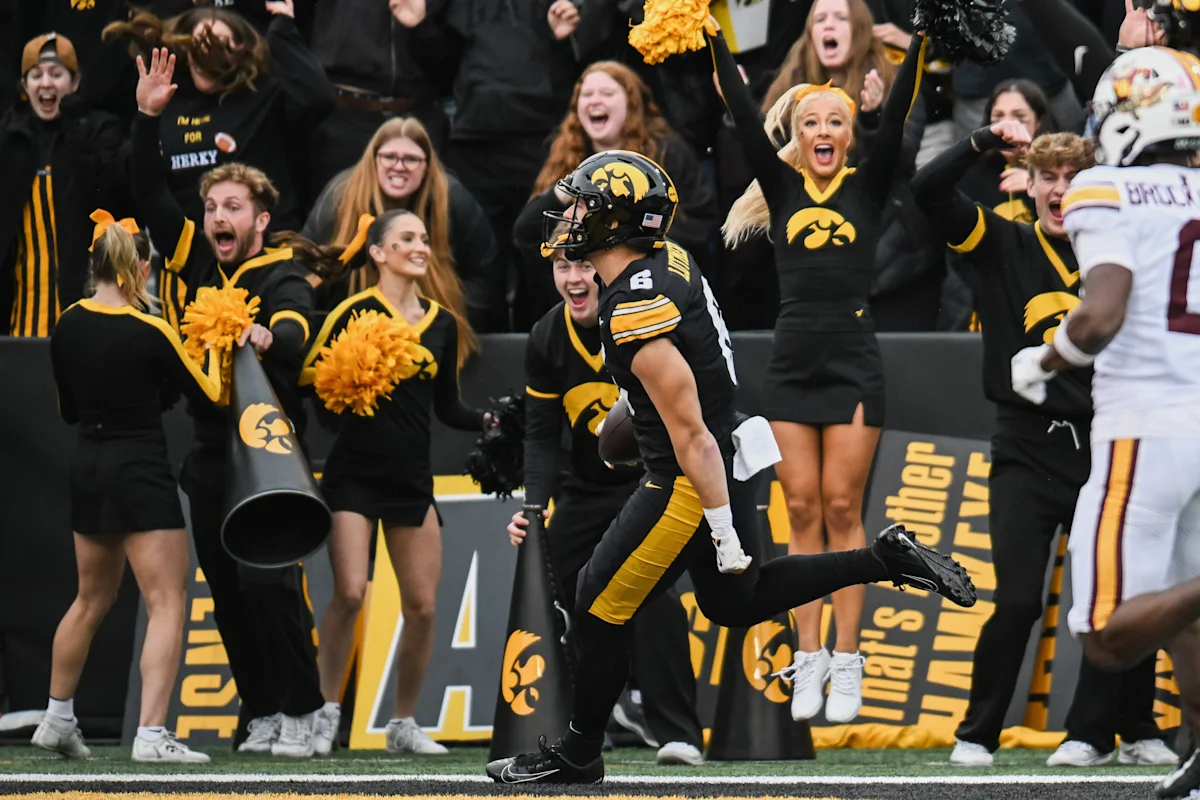 Iowa football player celebrates near sideline as cheerleaders and fans react during a game.