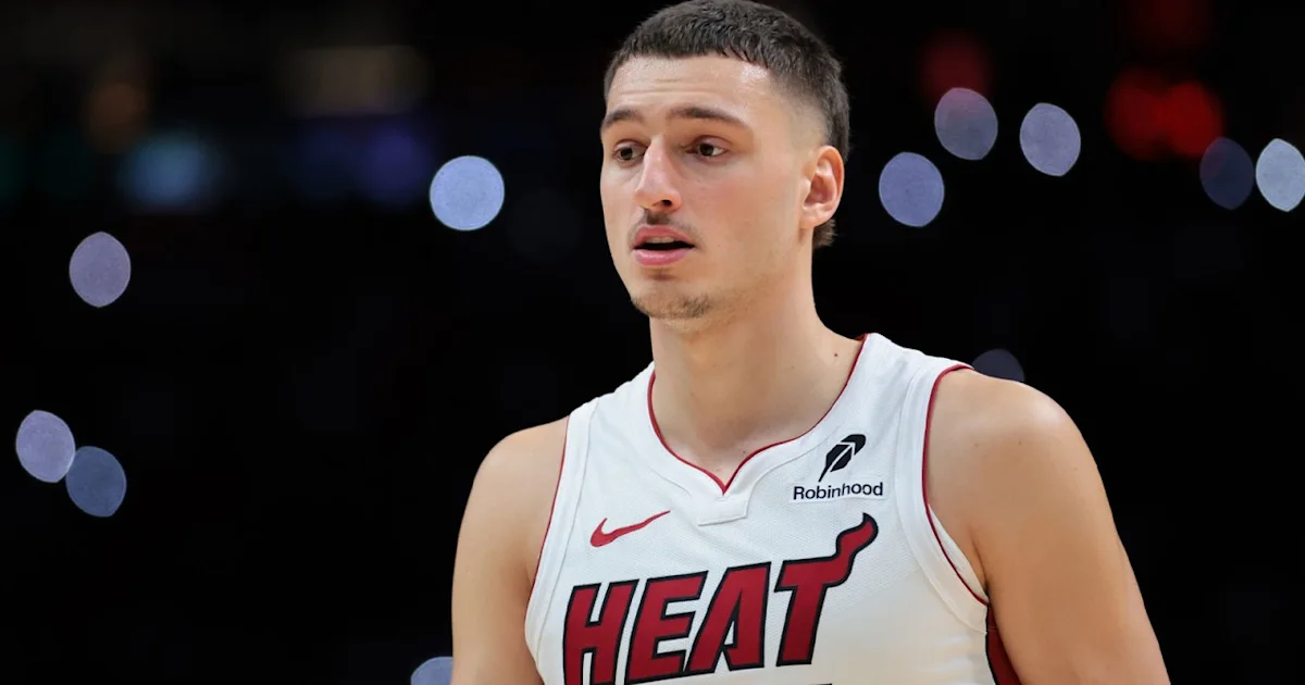 A Miami Heat player in a white jersey looks to the side against a dark, blurred arena background.