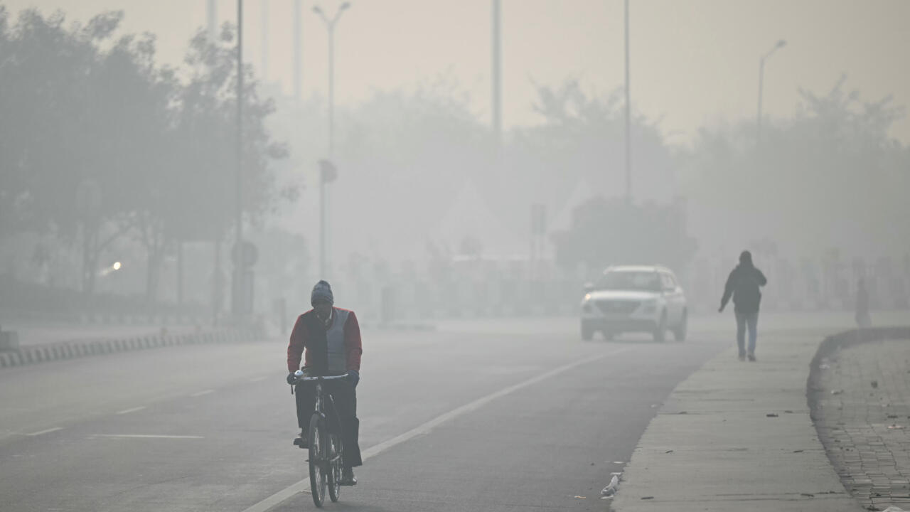 A cyclist rides along a hazy road as a car and pedestrian emerge through the smog.