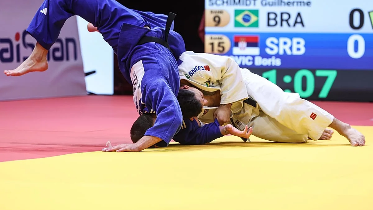 Judo athletes in blue and white gis grapple on a yellow and red mat.
