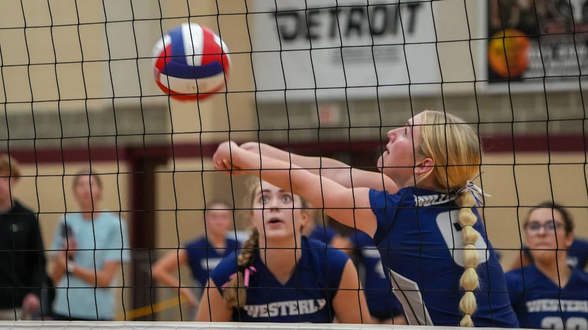 A volleyball player in a blue jersey bumps the ball over the net as teammates watch.