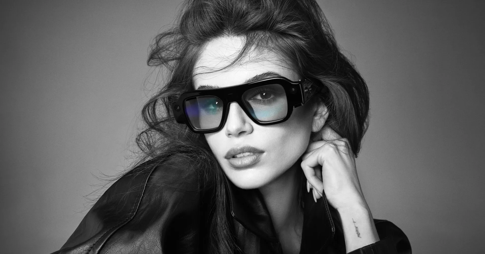 Black-and-white portrait of a woman wearing large smart glasses and a dark jacket