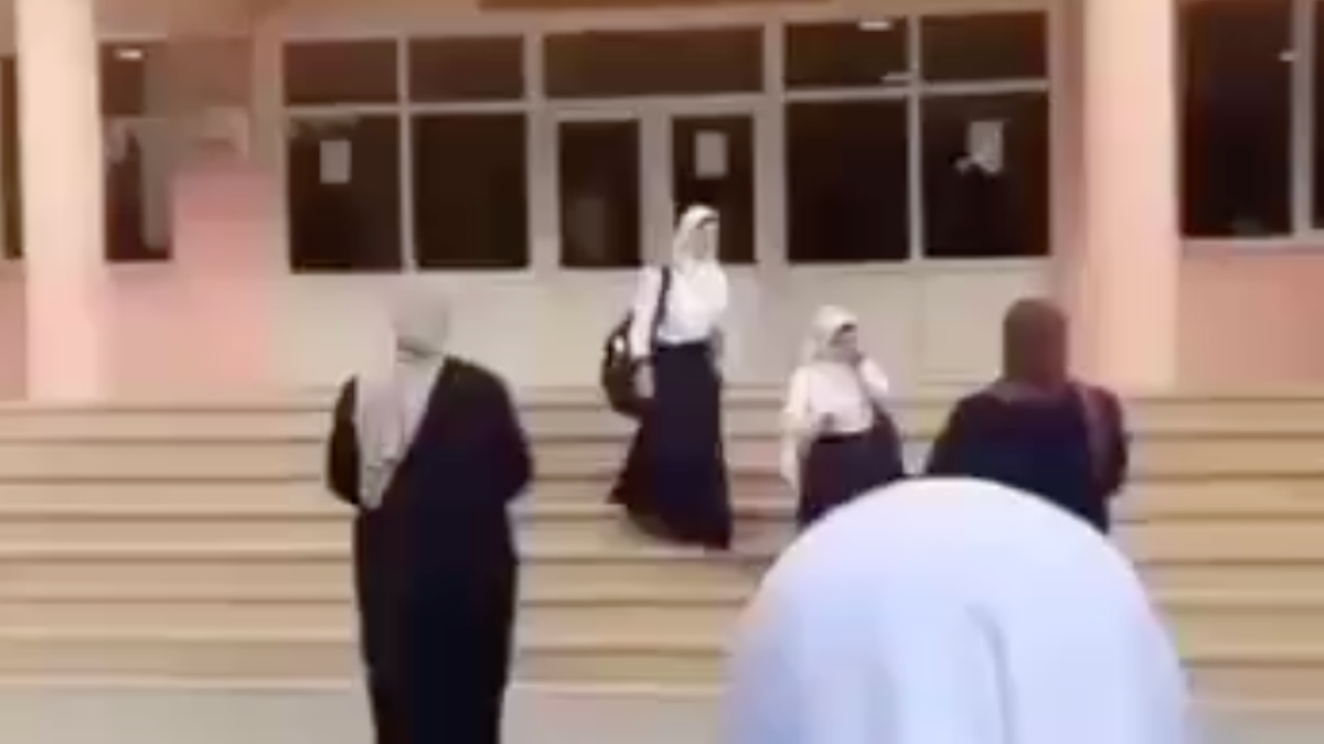 Several women in headscarves and dark clothing stand on steps outside a building.