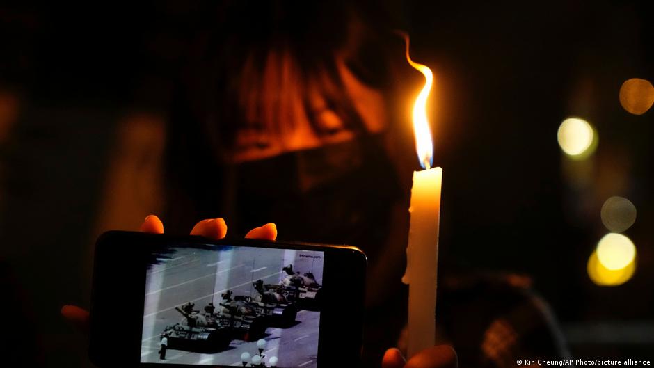 Person holds a candle and smartphone displaying footage of tanks in a dark setting.