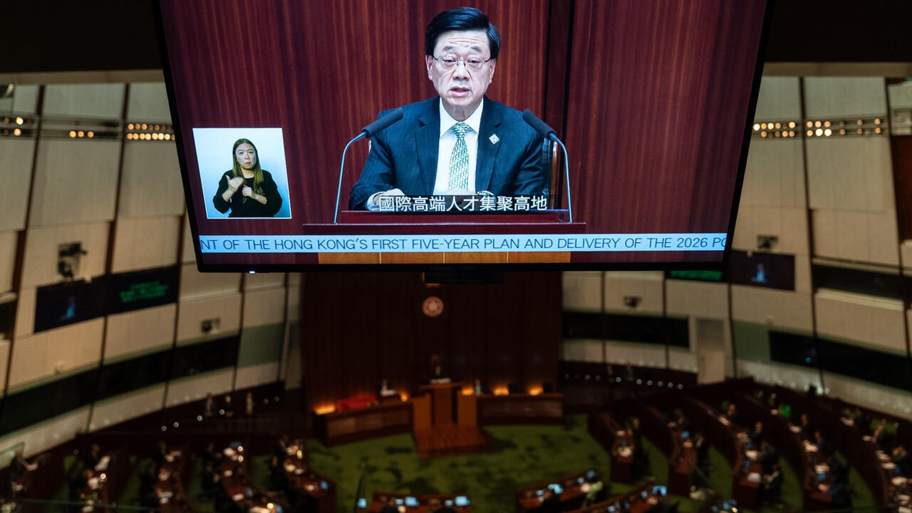 Large screen shows a Hong Kong official speaking in a legislative chamber with a sign-language interpreter inset.