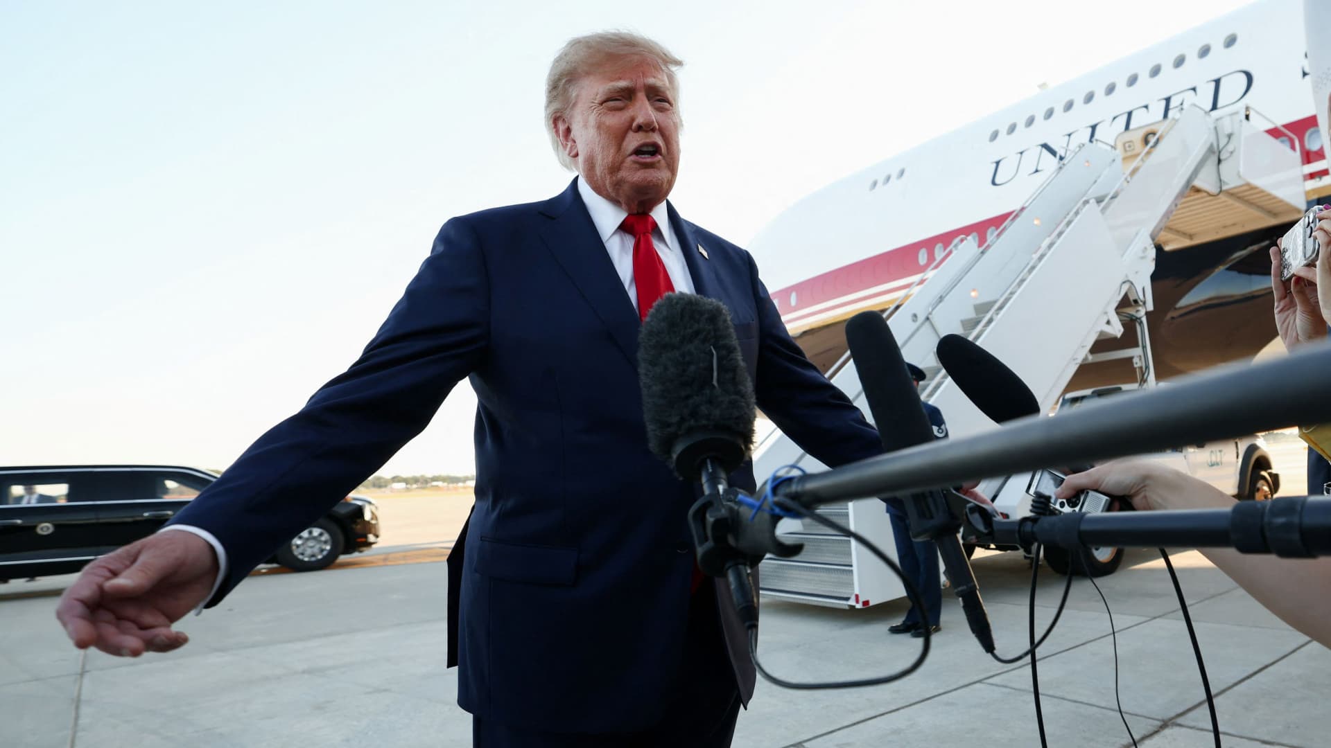 Donald Trump speaks to reporters beside Air Force One as microphones are held toward him.