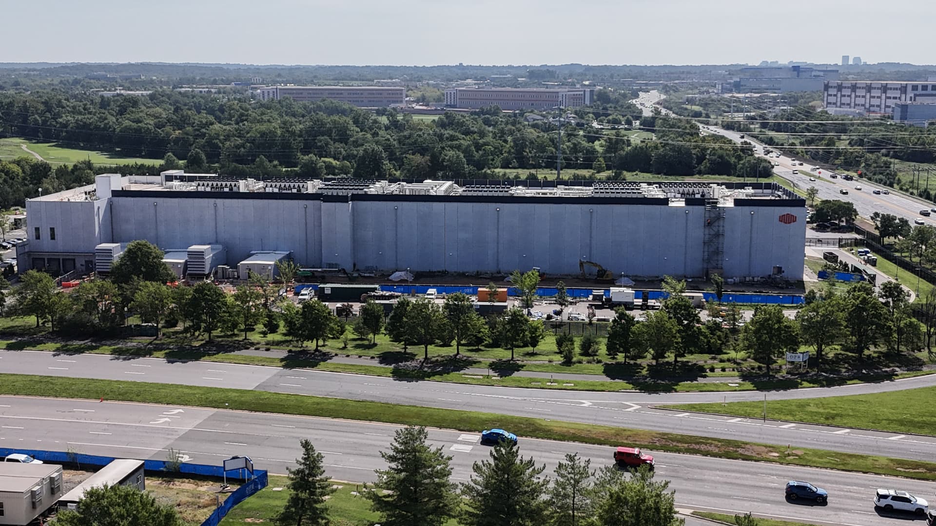 Large industrial data center building beside multilane highways, trees, and surrounding office complexes