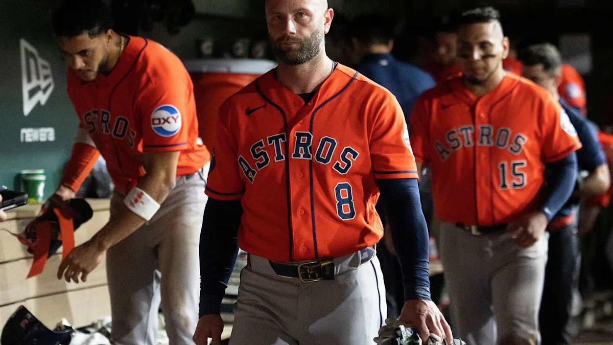 Houston Astros players in orange uniforms walk through a dugout, with one player carrying equipment.