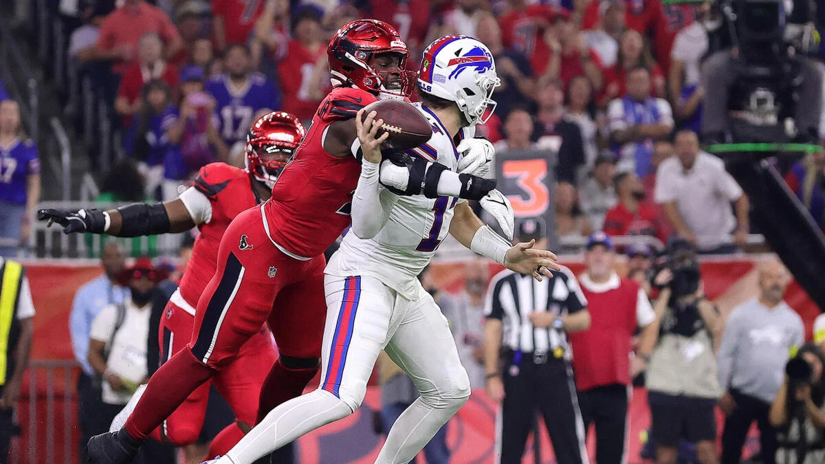 Football quarterback in white is hit by a red-uniformed defender while holding the ball.