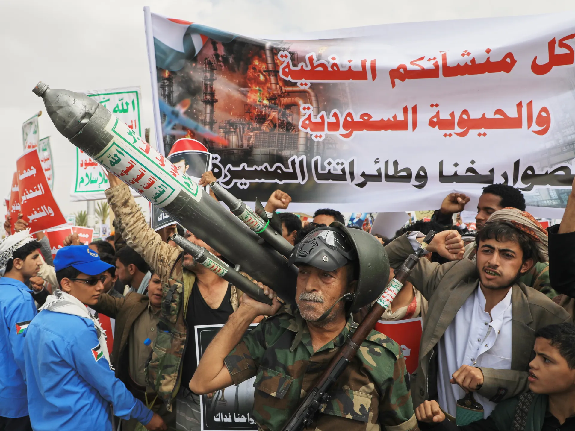 Crowd of demonstrators holding a large rocket-shaped object beneath Arabic banners