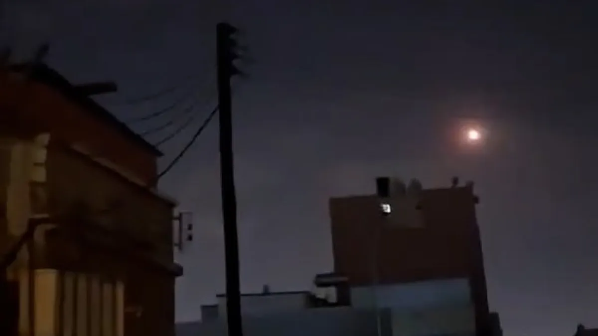 Nighttime view of silhouetted buildings, utility wires, and a bright moon in a hazy sky.