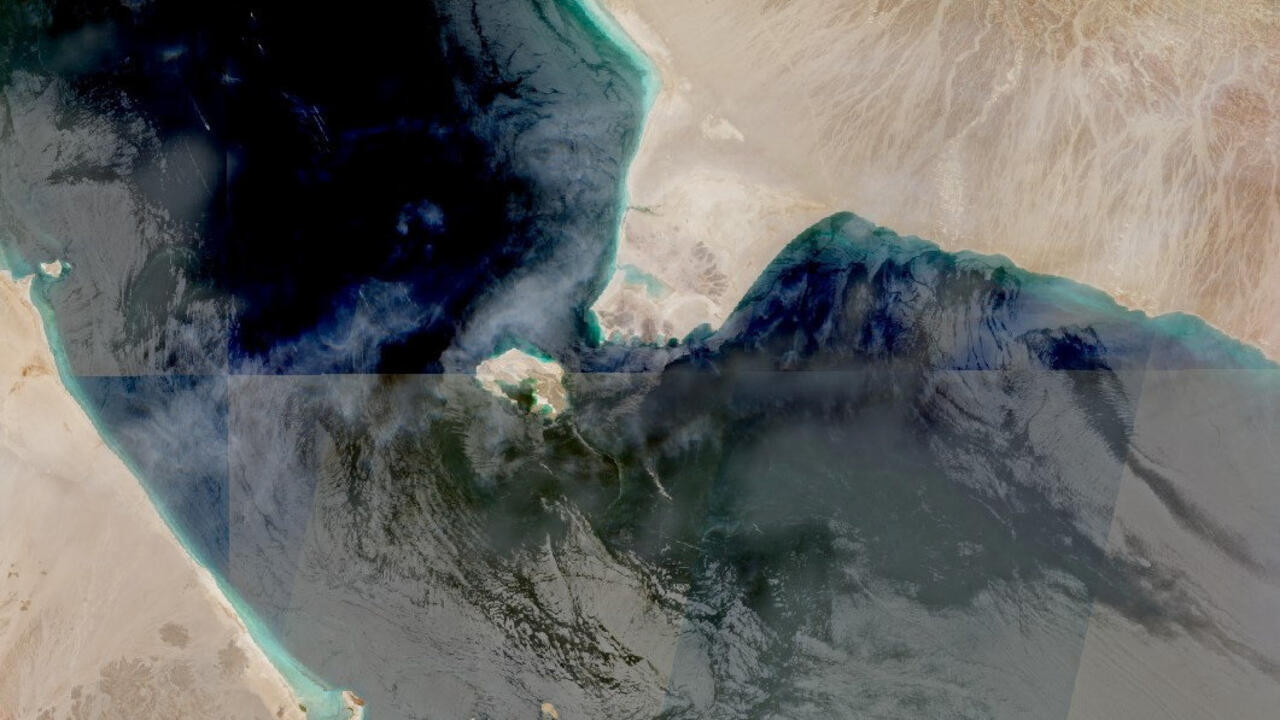 Satellite-style image showing dark blue water, turquoise coastal shallows, and surrounding sandy desert terrain