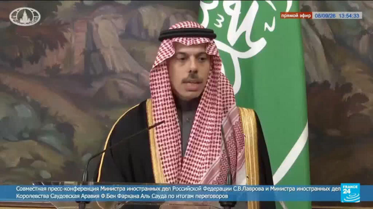 Saudi official in traditional dress speaking at a televised press conference beside a Saudi flag