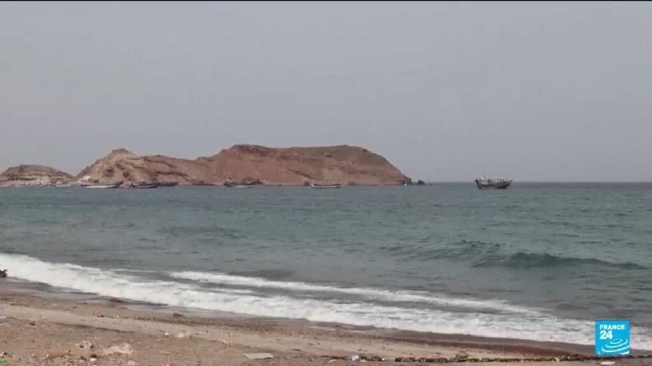 Small rocky island and fishing boats visible beyond waves from a sandy shoreline