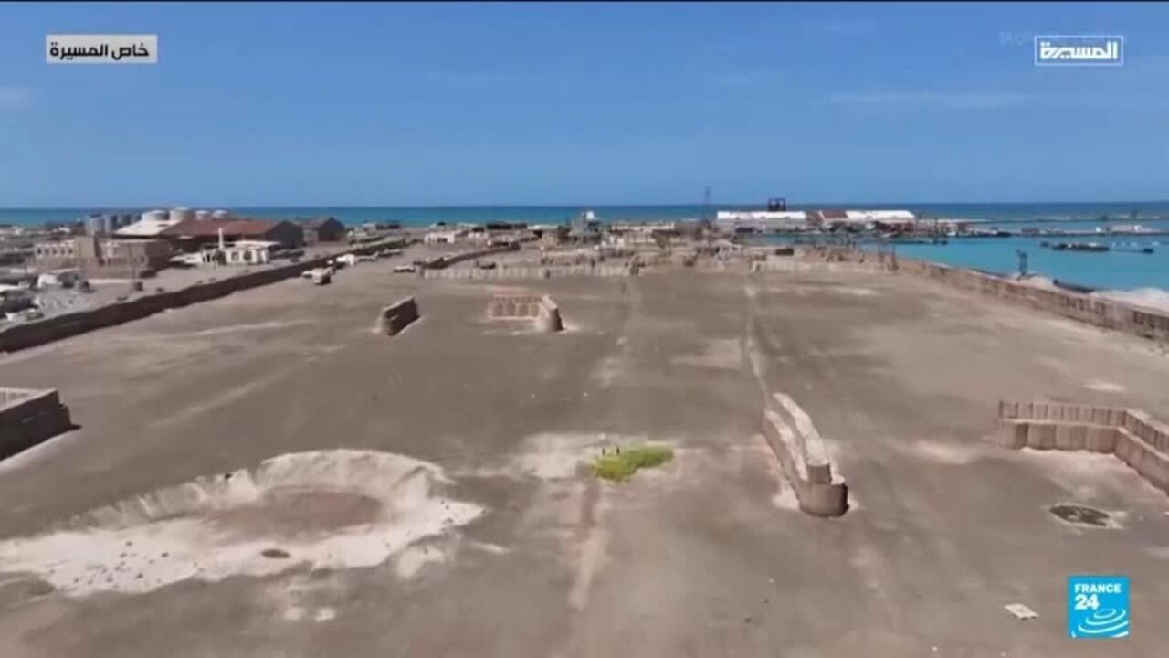Aerial view of a barren coastal compound beside turquoise waters and the open sea.