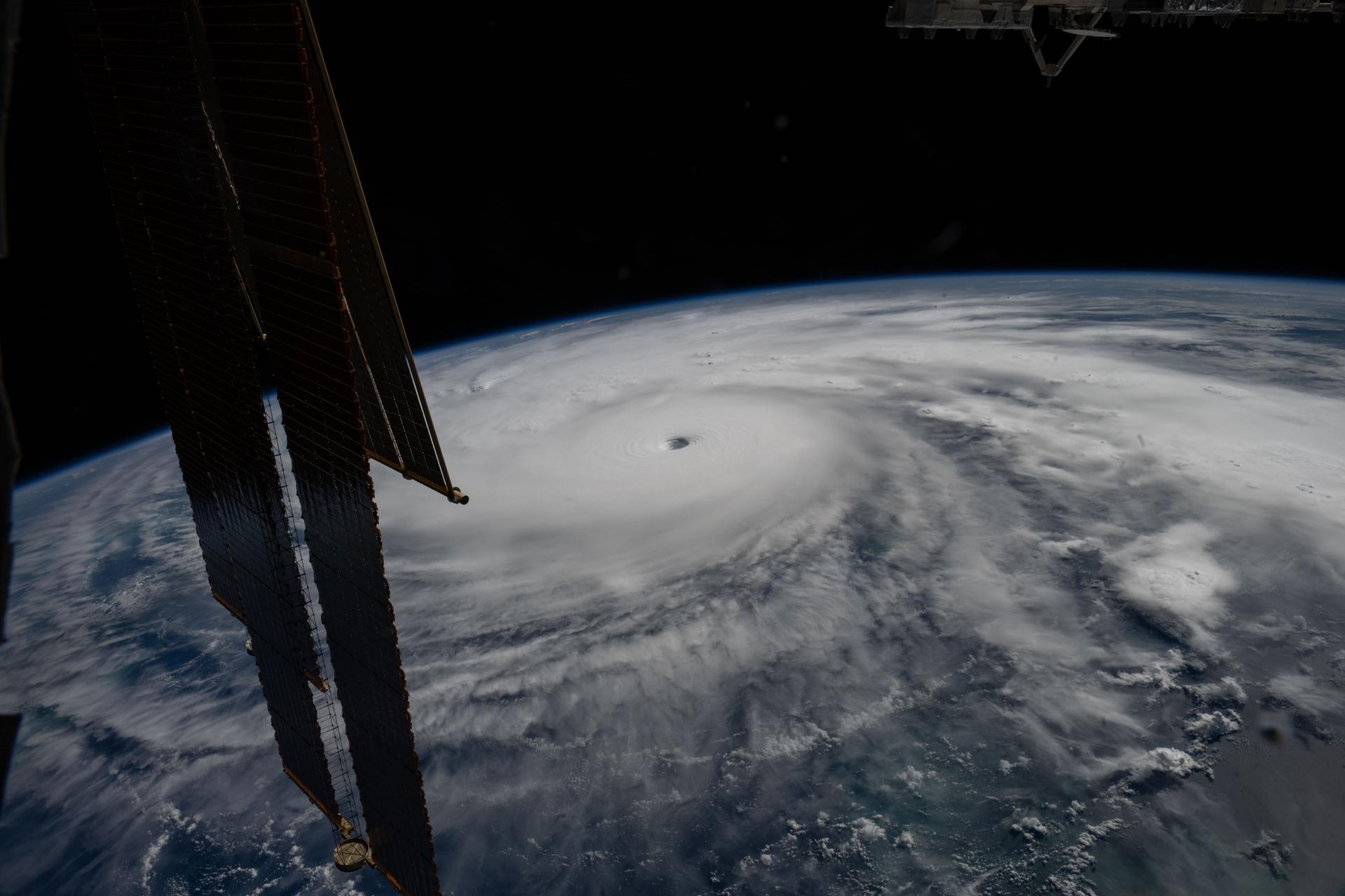 Satellite solar panel frames a large swirling hurricane over Earth’s cloud-covered surface.