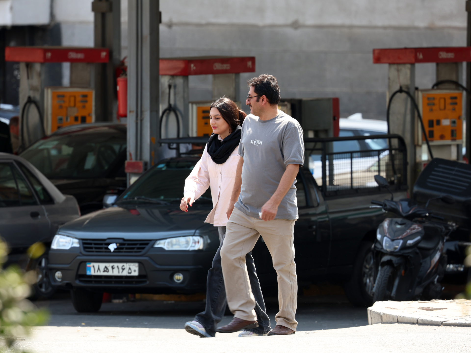 A couple walks past parked cars and service bays at an automotive repair garage.