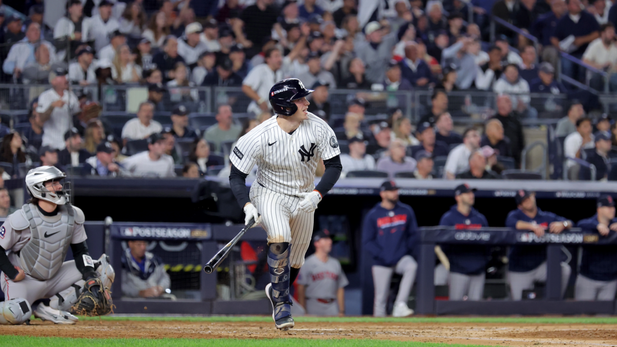 Yankees batter in pinstripes walks near home plate as a catcher crouches and players watch from the dugout.