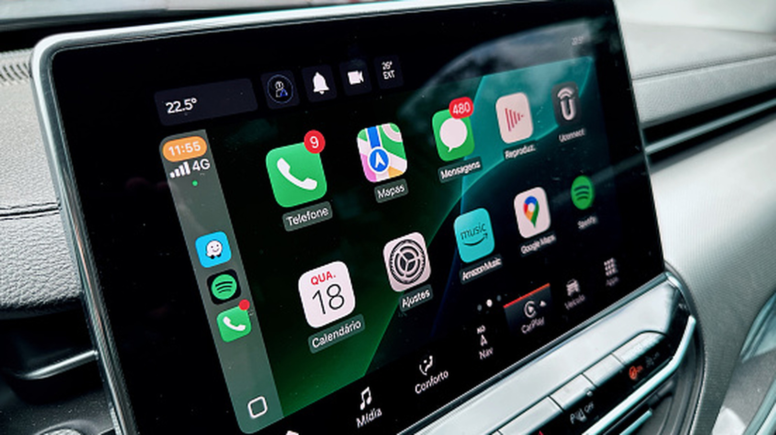 Car dashboard touchscreen displaying Apple CarPlay-style app icons, navigation, phone, messaging, and music controls.