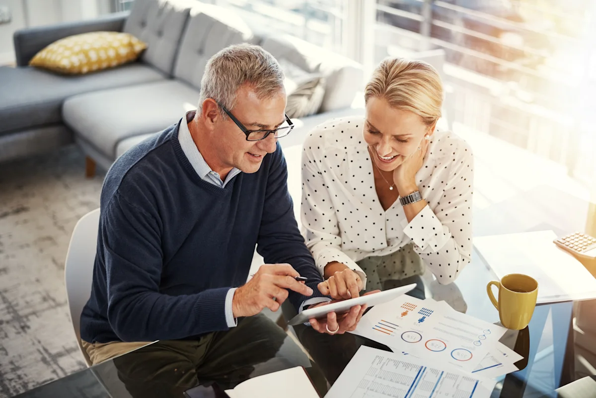 Older couple reviewing financial charts and a tablet together at a sunlit table