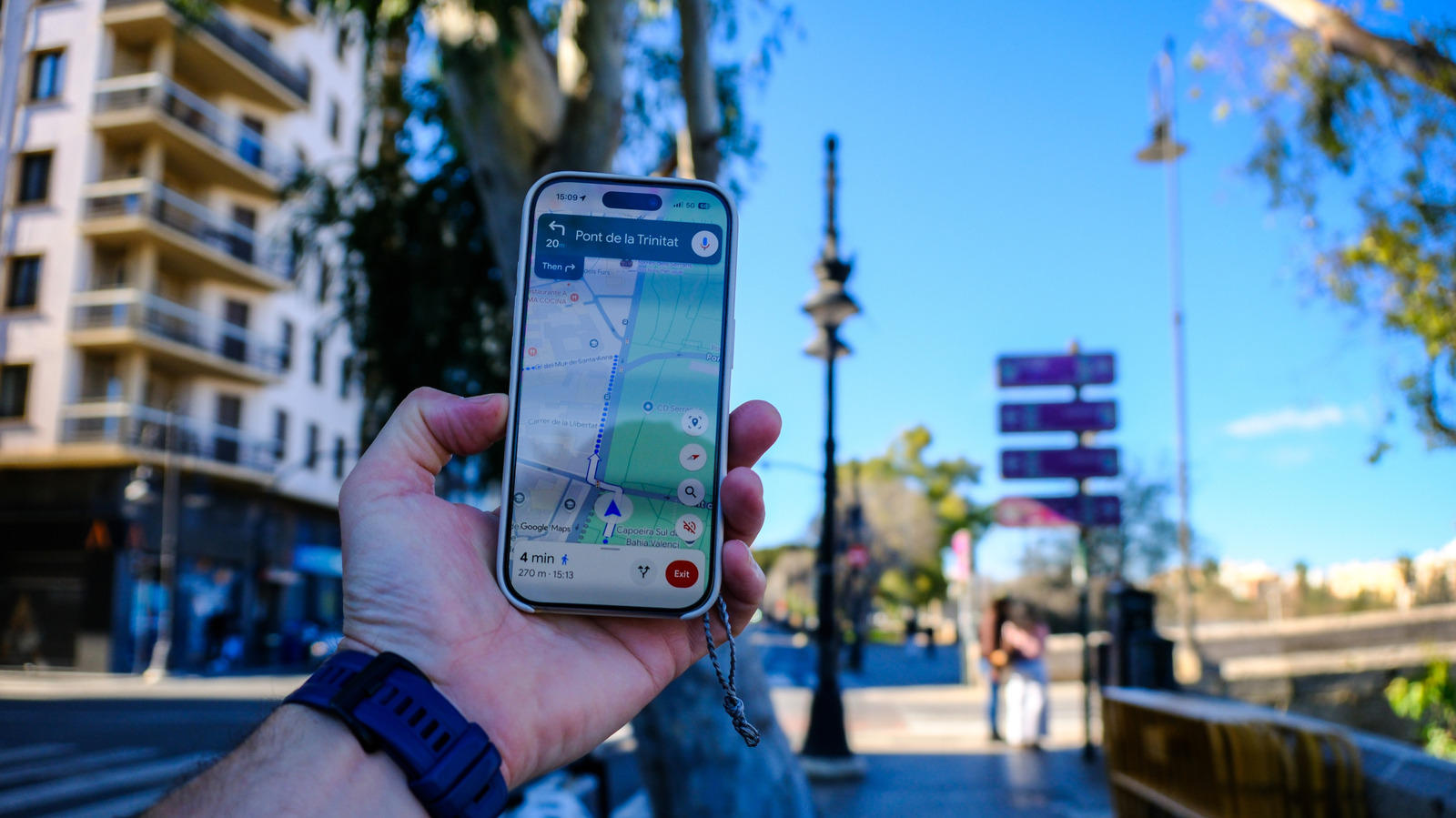 Hand holding smartphone displaying Google Maps navigation near a bridge and urban street