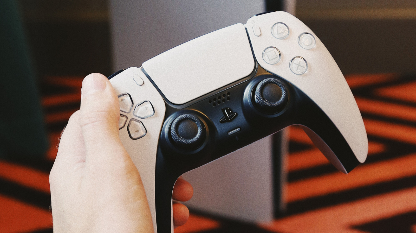 A hand holds a white and black PlayStation 5 DualSense wireless controller.