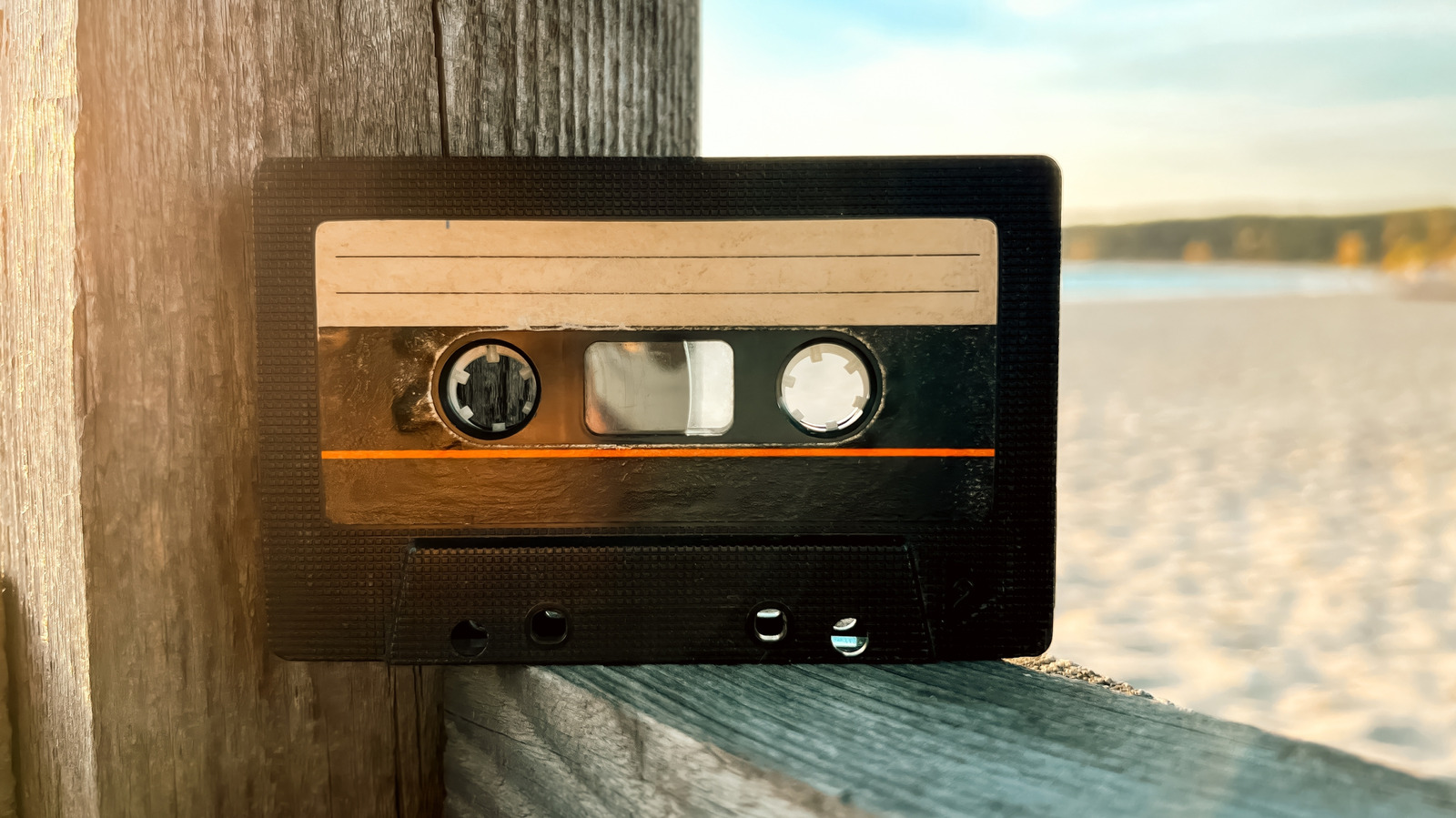 Close-up of a vintage cassette tape resting on a weathered wooden railing beside water.