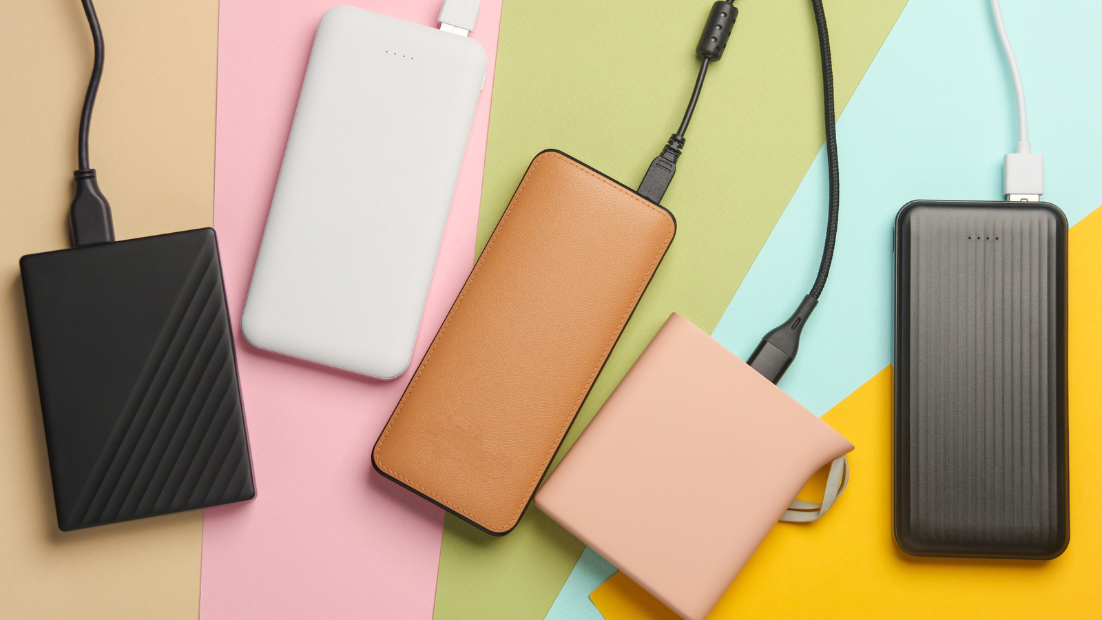 Several power banks in different colors and designs arranged on a pastel background, with cables attached.