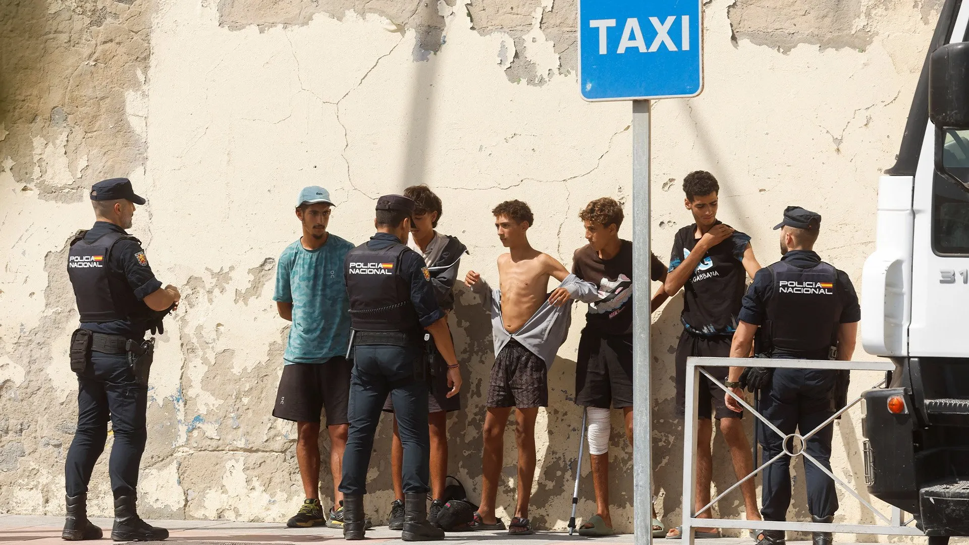 Police officers stand beside several young men near a taxi sign and white vehicle.
