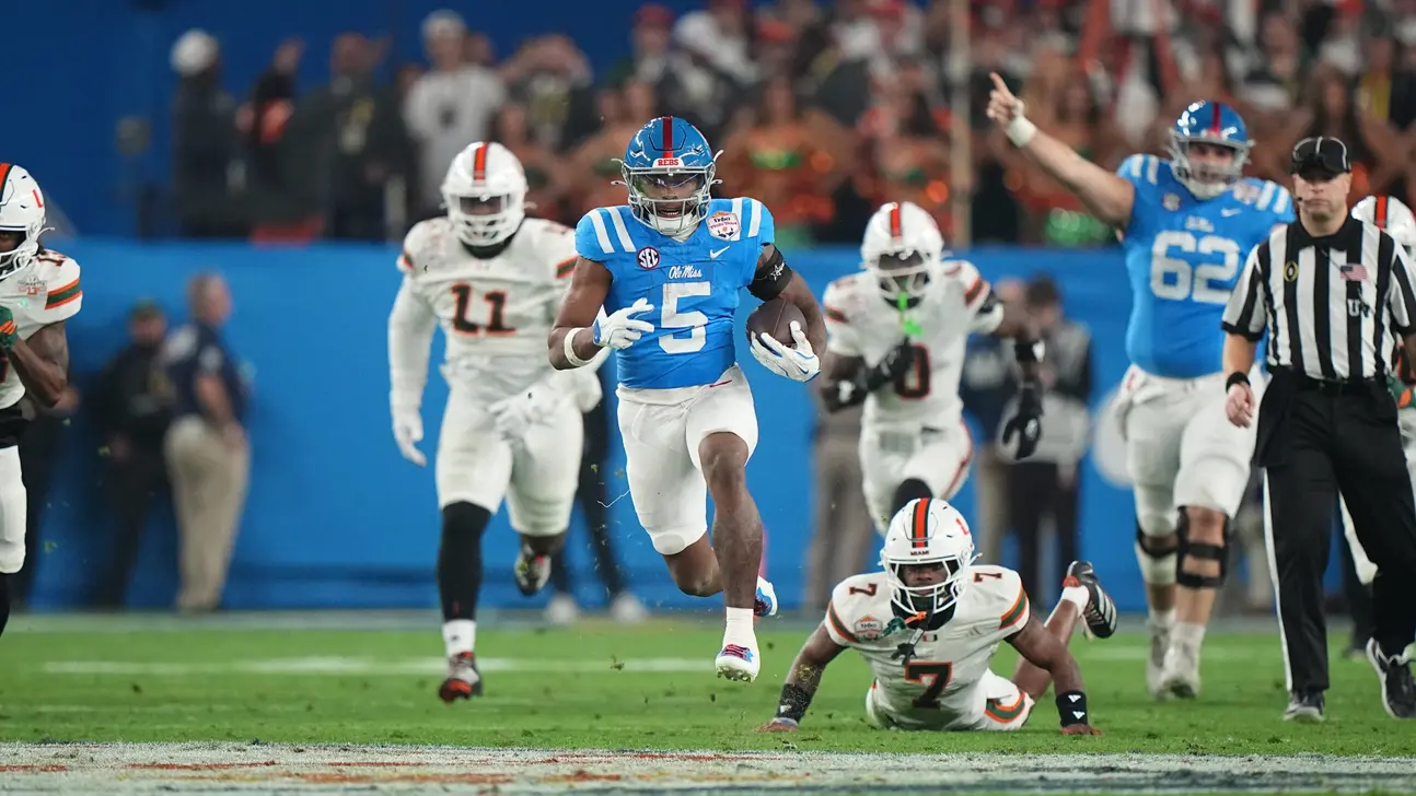 Ole Miss football player runs with the ball as defenders pursue on the field