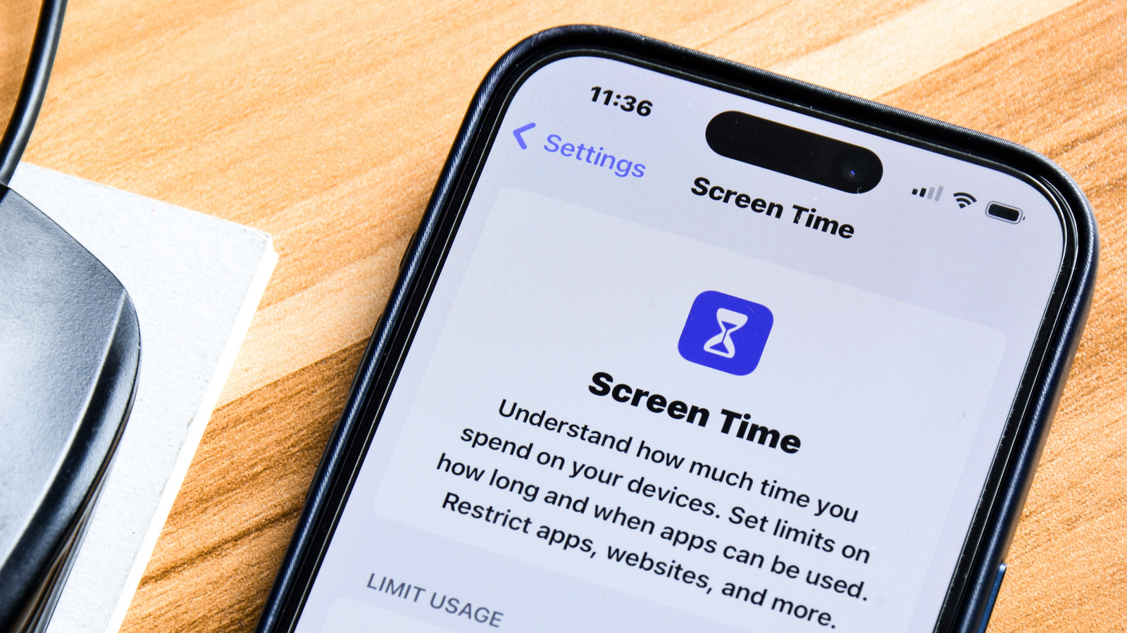 Close-up of an iPhone displaying the Screen Time settings page on a wooden desk.