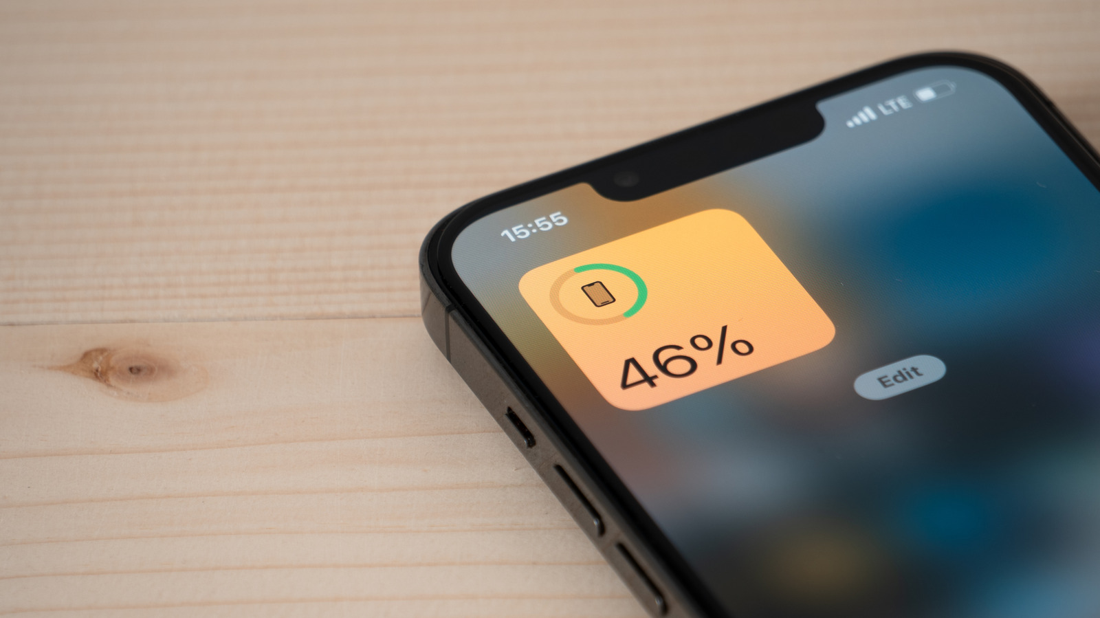 Close-up of an iPhone displaying a 46% battery widget on a wooden surface