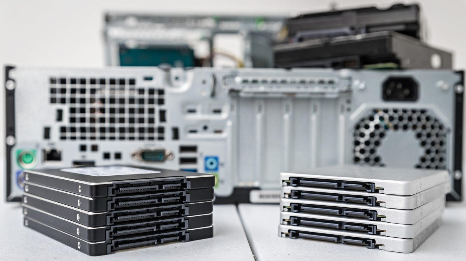 Stacks of black and silver hard drives sit in front of an open desktop computer case.