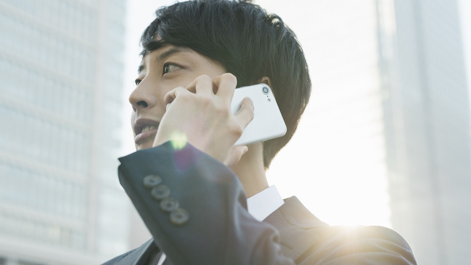 A man in a suit holds a white smartphone to his ear in bright daylight.