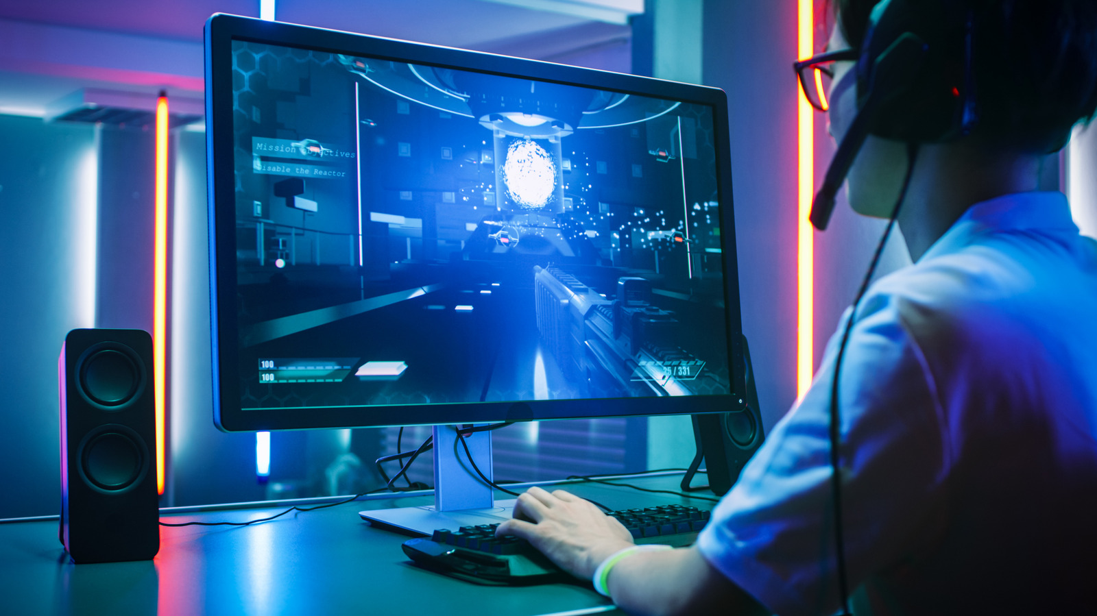 A person wearing a headset plays a first-person shooter on a desktop computer in blue and pink lighting.