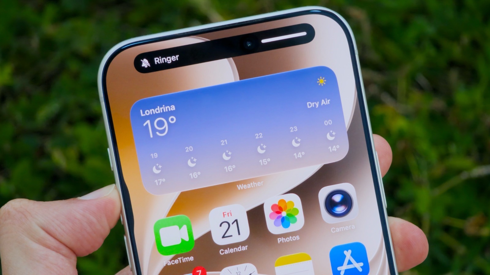 Close-up of an iPhone displaying a weather widget and a muted Ringer notification while held outdoors.