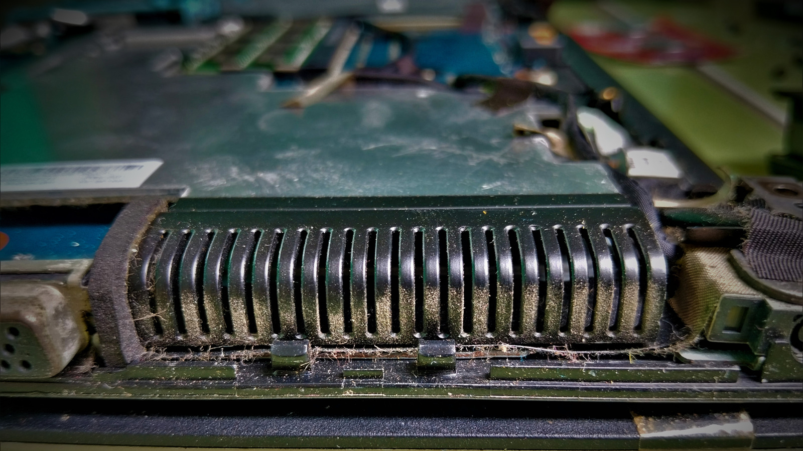 Close-up of a dusty laptop fan vent and internal components with lint and debris along the edges.