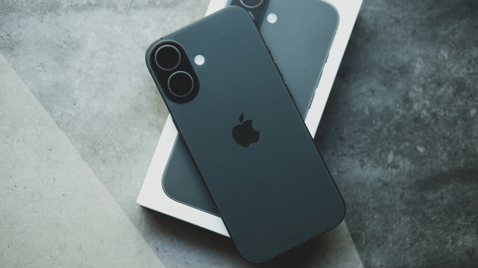Two dark iPhones rest diagonally on a white box against a textured gray surface.
