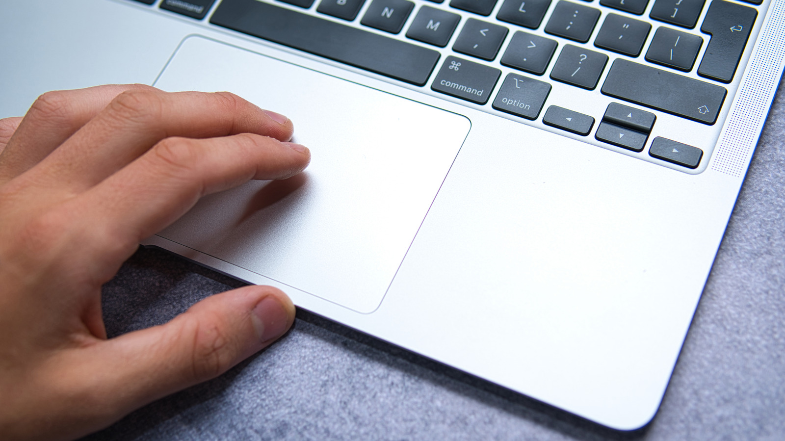 Hand using the trackpad on a silver MacBook beside the keyboard