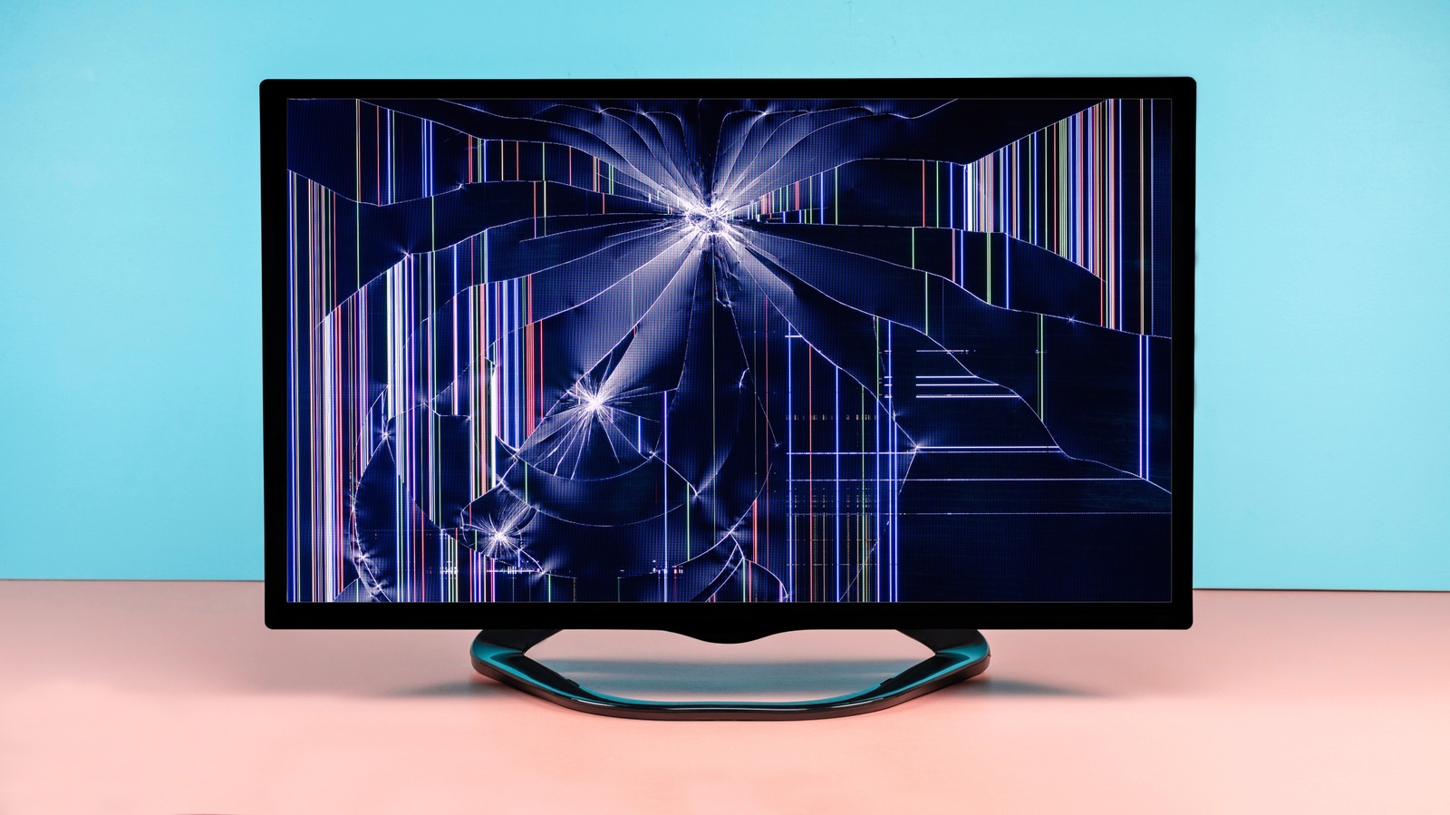 Flat-screen monitor displaying a severely cracked screen with colorful vertical lines on a pink surface