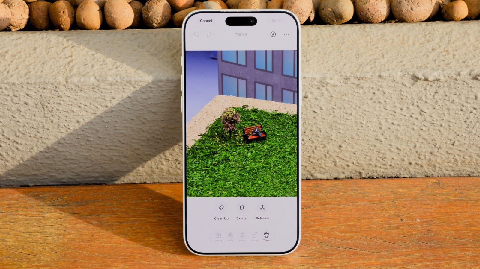 iPhone displaying Apple Photos Clean Up tool over a miniature park scene with grass, bench, and tree.