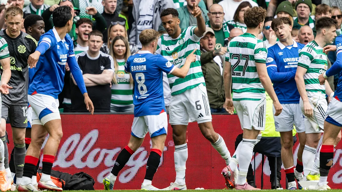 Celtic and Rangers players gather during a tense football match as supporters watch.