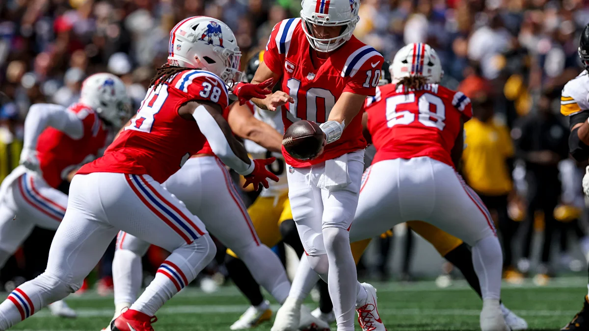 Patriots players in red and white uniforms exchange the football during a game.